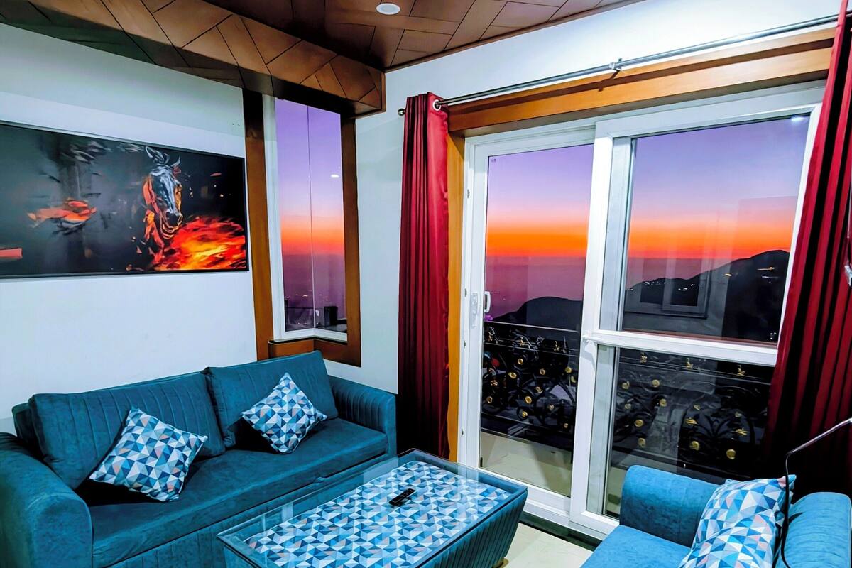 Un soggiorno moderno con un divano blu, un tavolino da caffè decorato, una ventola a soffitto e un'ampia finestra con vista sulla città.