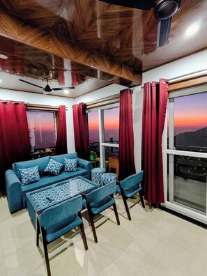 A modern living room with a sofa, chairs, a coffee table, and a large window with curtains. - Opal Villas (Mussoorie)