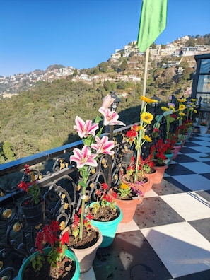 A balcony with potted plants and a view of a hillside town. - Opal Villas (Mussoorie)