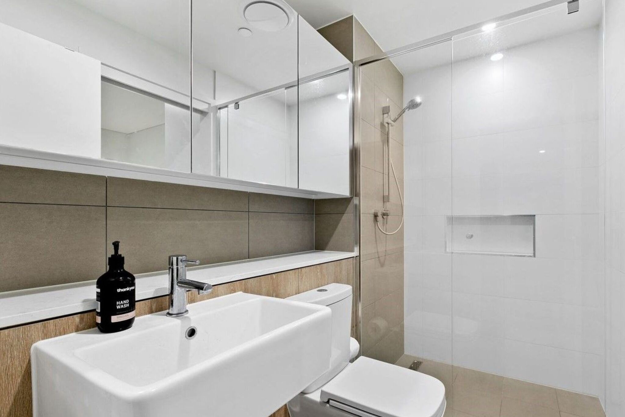 A modern bathroom with a white sink, a toilet, and a glass-enclosed shower.