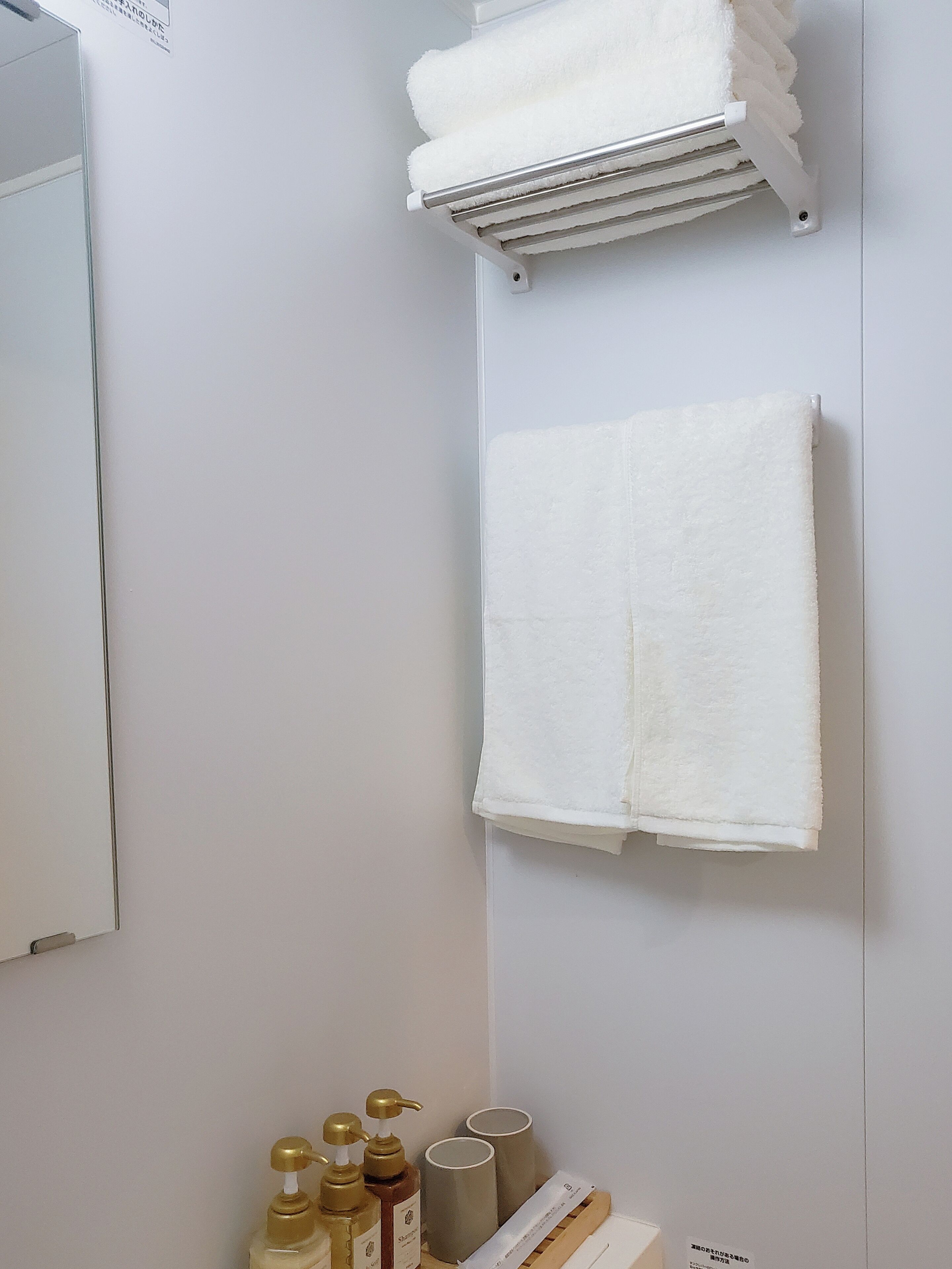 Un baño con un perchero que sostiene dos toallas blancas, un espejo y un estante con artículos de aseo personal, incluyendo botellas y un recipiente.