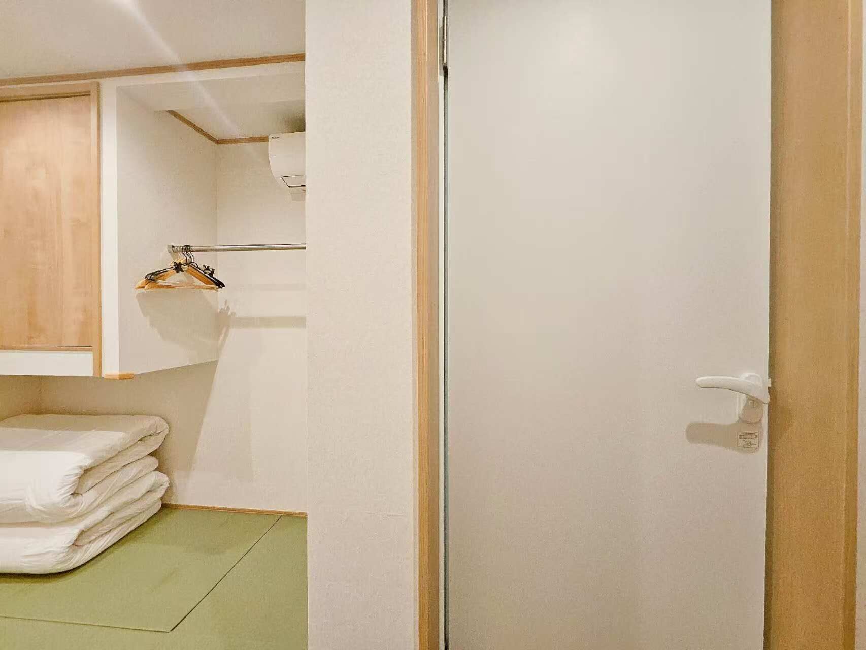 A room with a wooden cabinet, a hanging towel rack, and a neatly folded stack of towels on the floor.