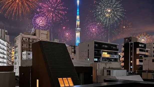 Una terraza en la azotea con vistas a un horizonte urbano, incluyendo una torre y fuegos artificiales.