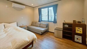 Un dormitorio con cama, una zona de descanso pequeña, una ventana con cortinas, un estante empotrado y un aire acondicionado instalado en la pared.