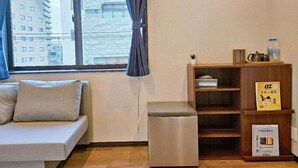 Una habitación pequeña y moderna con sofá, una mesita, una estantería y una ventana con cortinas.