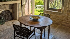 Una habitación con paredes de piedra, una mesa redonda de madera, dos sillas, una lámpara colgante y una ventana con vistas a la vegetación.