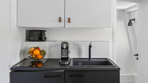 A kitchen with white cabinets, a black countertop, a fruit bowl, a coffee maker, and a sink.
