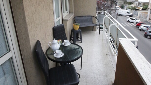 Un balcón con una mesa preparada para dos personas, una silla, un ventanal y vista a la calle.