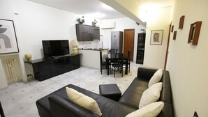 Una sala de estar moderna con un sofá de cuero negro, un televisor de pantalla plana y un comedor con mesa y sillas.