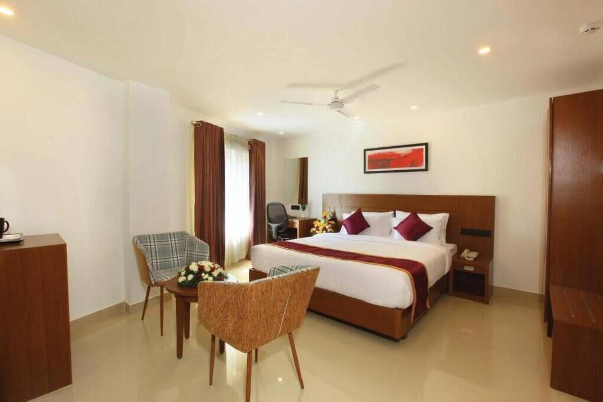 A hotel room with a large bed, a desk with a chair, a small table with a chair, and a ceiling fan.