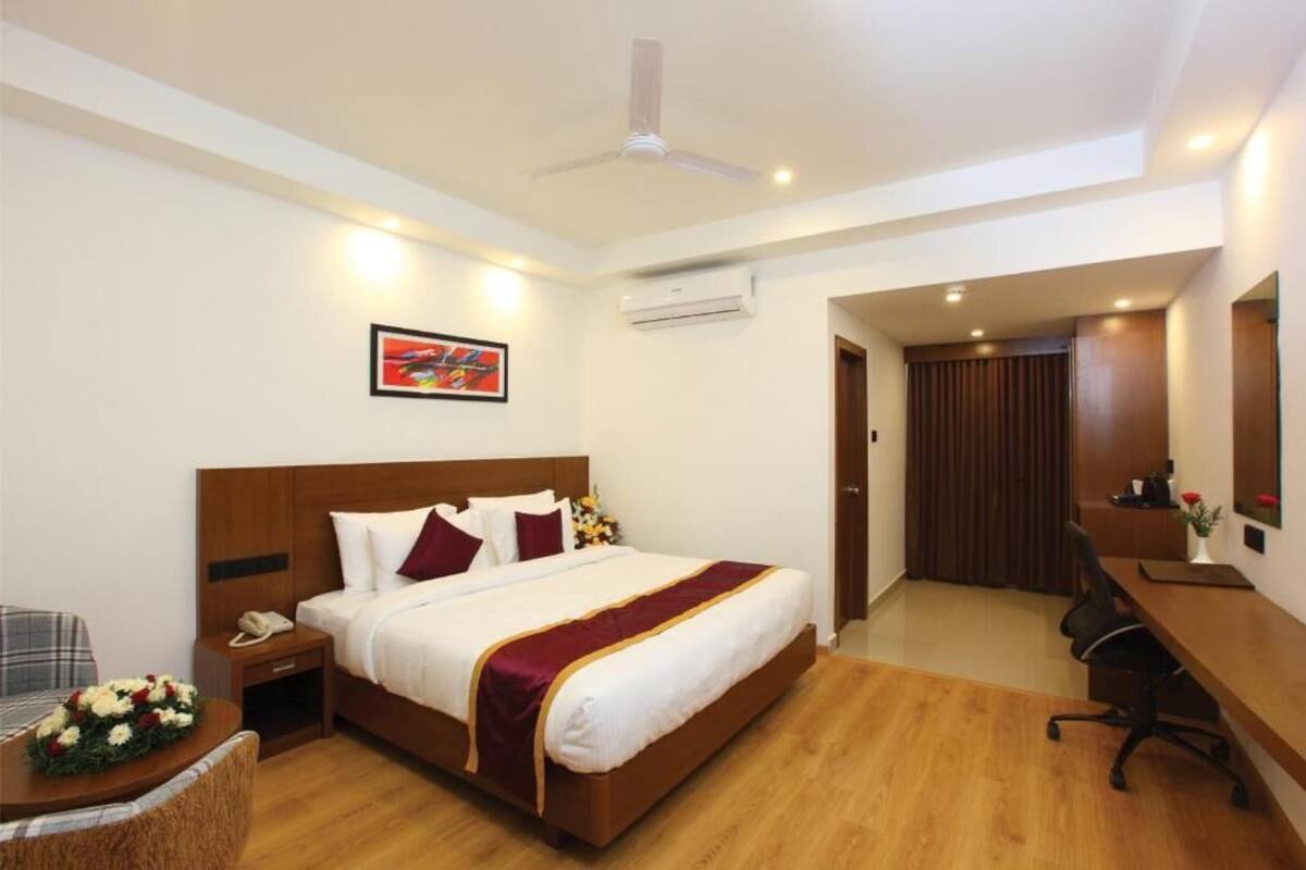 A hotel room with a large bed, a desk, a chair, a telephone, and an air conditioning unit.