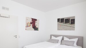 Ein Schlafzimmer mit einem Bett, weißen Wänden und zwei Bildern an der Wand.
