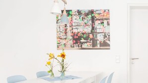 Ein weißer Esstisch mit zwei Blumenvasen, einer hängenden Pendelleuchte und einem farbenfrohen, abstrakten Gemälde an der Wand.