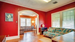 A room with a red wall, a wooden floor, a sofa, a table, and a lamp. - Walkable Dtwn Lafayette Home w/ Screened Porch (Lafayette)