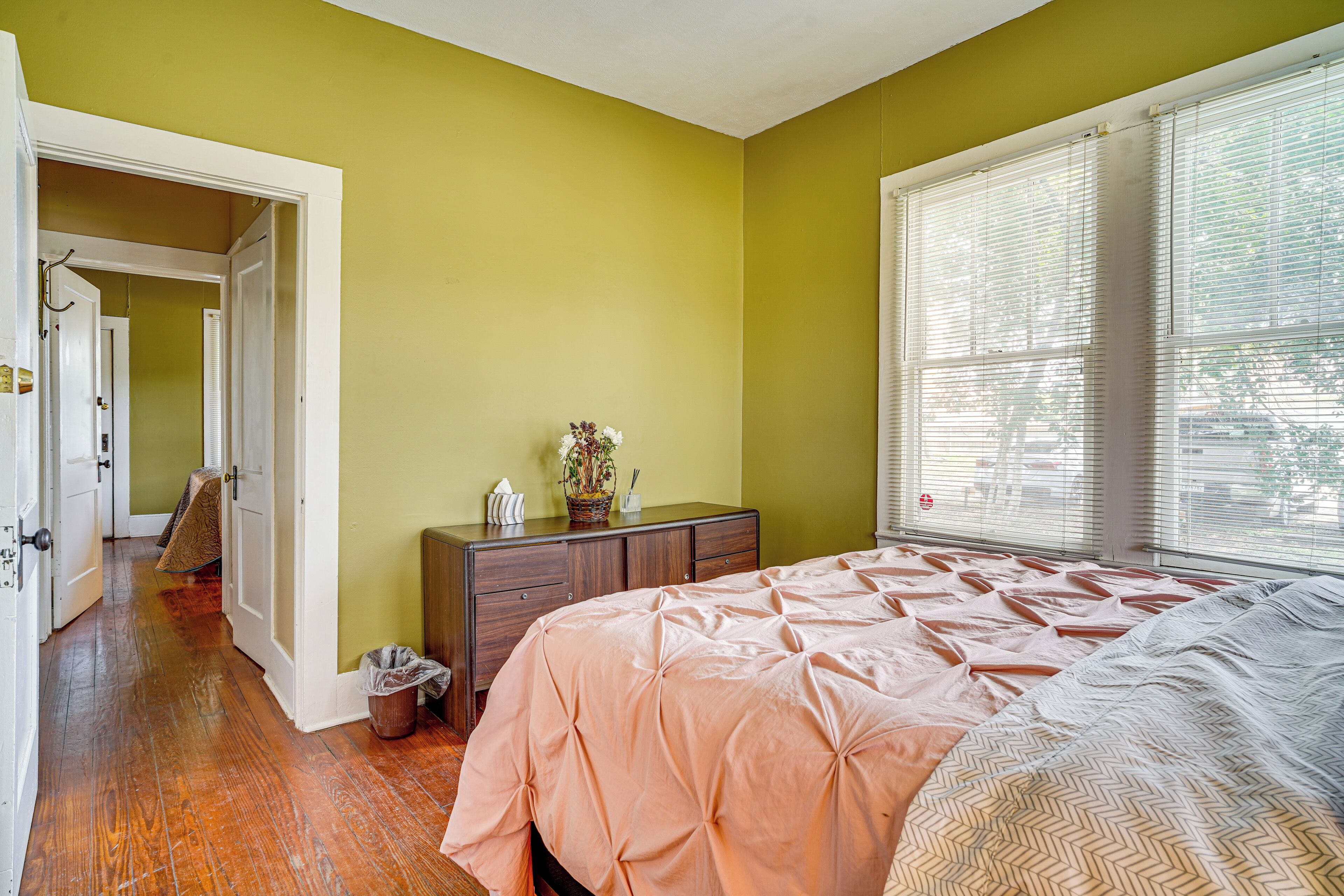 A bedroom with a bed, dresser, and a window with blinds.