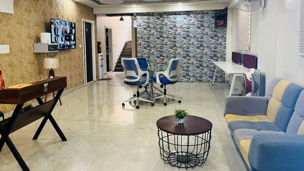 Un moderno vestíbulo de hotel con una zona de estar, un televisor montado en la pared y una escalera que conduce a otro piso.