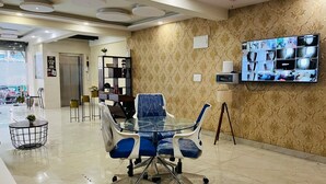Un salón de conferencias con una mesa de vidrio y sillas azules, un televisor montado en la pared y un papel tapiz estampado.