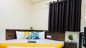 Una cama bien hecha con una manta amarilla, un cabecero de madera y una mesita de noche con una planta.