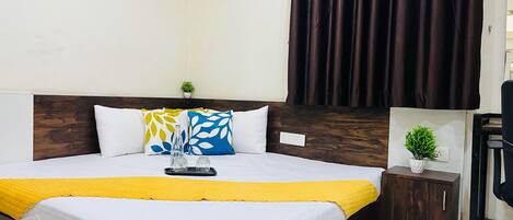 A neatly made bed with a yellow blanket, a wooden headboard, and a small bedside table with a plant.
