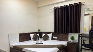 Un dormitorio ordenado con una cama grande, una mesita de noche con una planta, un escritorio con una silla y una ventana con cortinas.