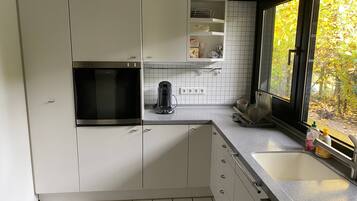 A modern kitchen with white cabinets, a built-in microwave, a coffee maker, and a window with a view of trees.