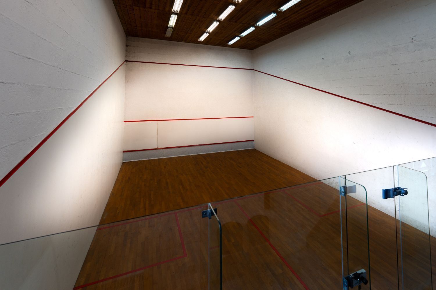 Un court de squash doté d’un plancher en bois et de parois en verre.
