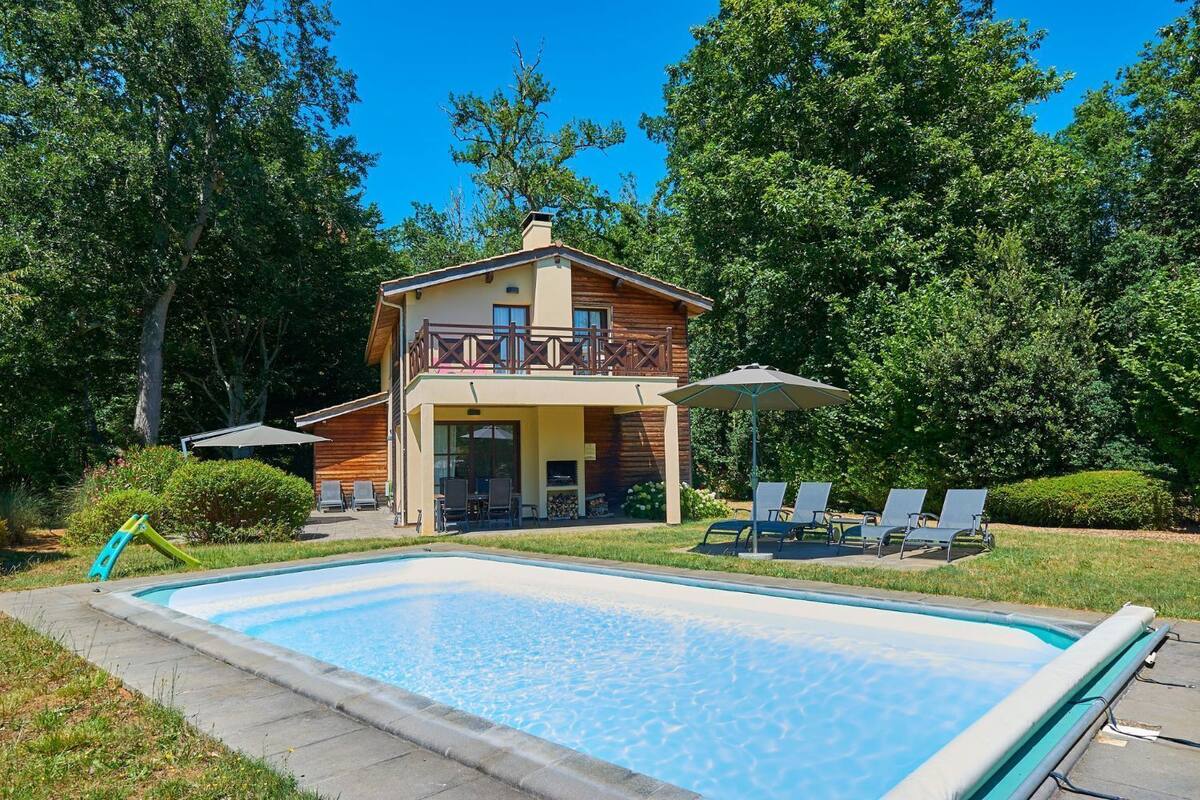 A two-story wooden house with a balcony, a swimming pool, and outdoor seating.