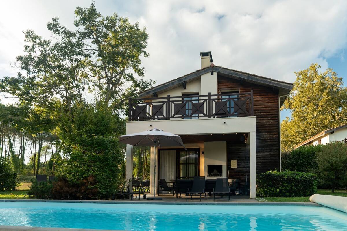 A two-story house with a swimming pool, outdoor seating, and a wooden deck.