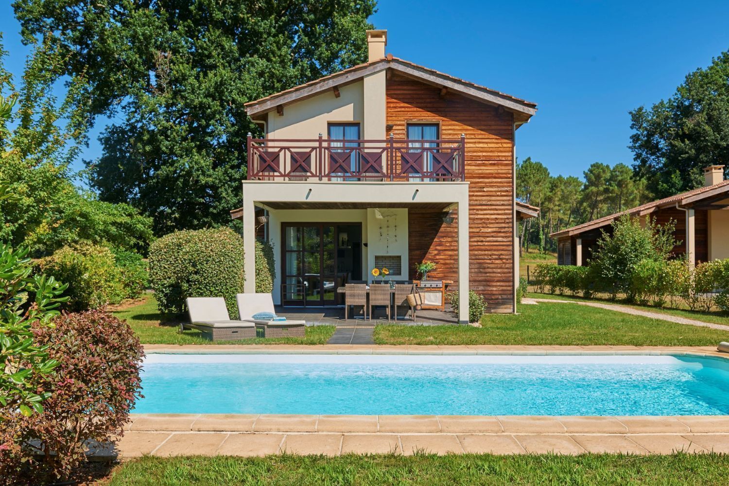 A two-story house with a balcony, a swimming pool, and a garden.