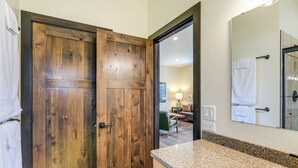 A bathroom with a wooden door, a granite countertop, and a mirror.
