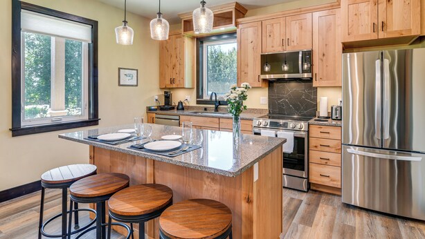 A modern kitchen with wooden cabinets, stainless steel appliances, a granite island, and bar stools.