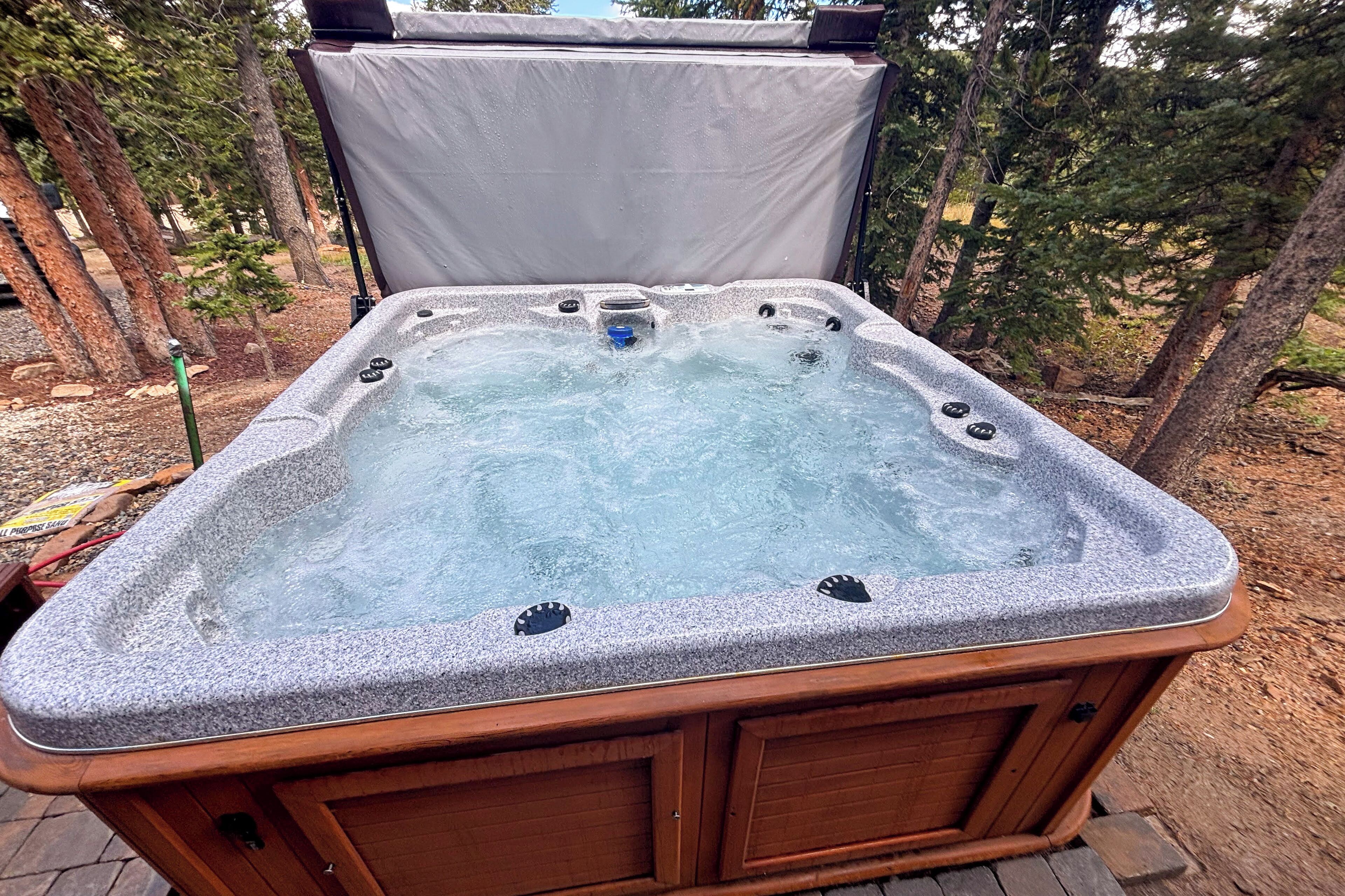 A hot tub with a wooden frame and a cover, surrounded by trees.