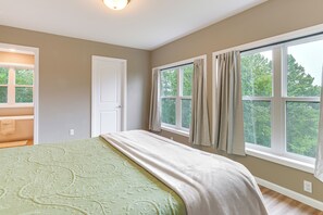 Un dormitorio con una cama grande, una ventana con cortinas y vistas a árboles.