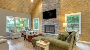 A living room with a stone fireplace, wooden ceiling, and large windows. - Modern Cabin w/ Sweeping Views in Blue Ridge Mtns! (Green Mountain)