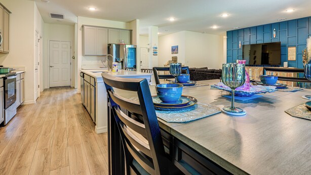 A modern kitchen with wooden flooring, a dining area with blue tableware, and a large TV on the wall. - Spacious Home Near Dtwn PSL: Travel Nurses Welcome (Port St. Lucie)