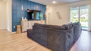 A modern living room with a dark grey sectional sofa, a wooden cabinet, and a blue accent wall. - Spacious Home Near Dtwn PSL: Travel Nurses Welcome (Port St. Lucie)