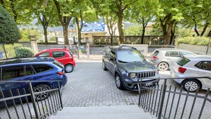 Ein Parkplatz mit mehreren in einer Reihe stehenden Autos, eine Treppe, die zu einem Gebäude führt, und Bäume, die Schatten spenden.