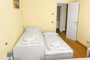 Una camera d'albergo piccola e singola con due letti, una porta che conduce a un'altra stanza e un lampadario fissato alla parete.