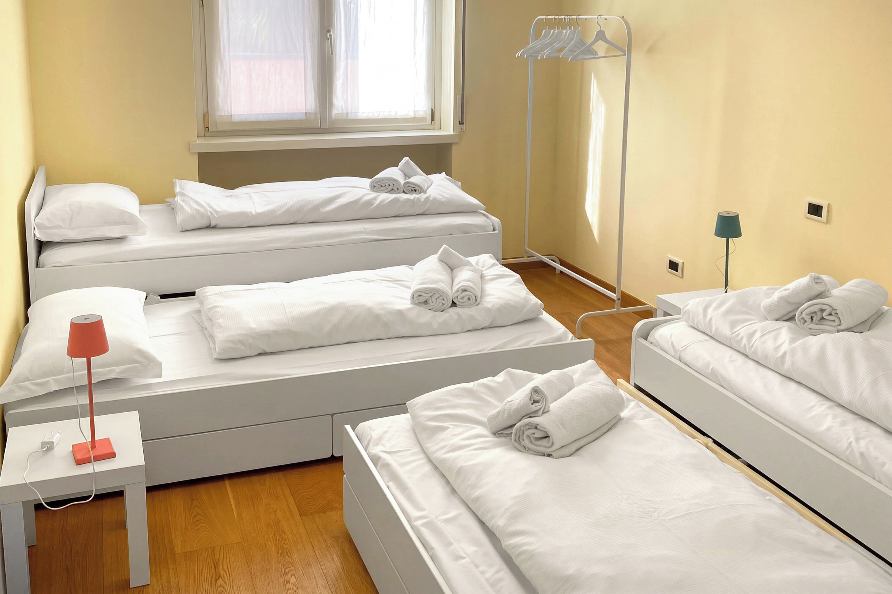 A hotel room with three single beds, a bedside table with a lamp, and a window with curtains.