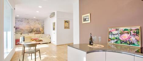A modern kitchen with a dining area, featuring a wooden floor, white cabinetry, and a large painting of flowers on the wall.