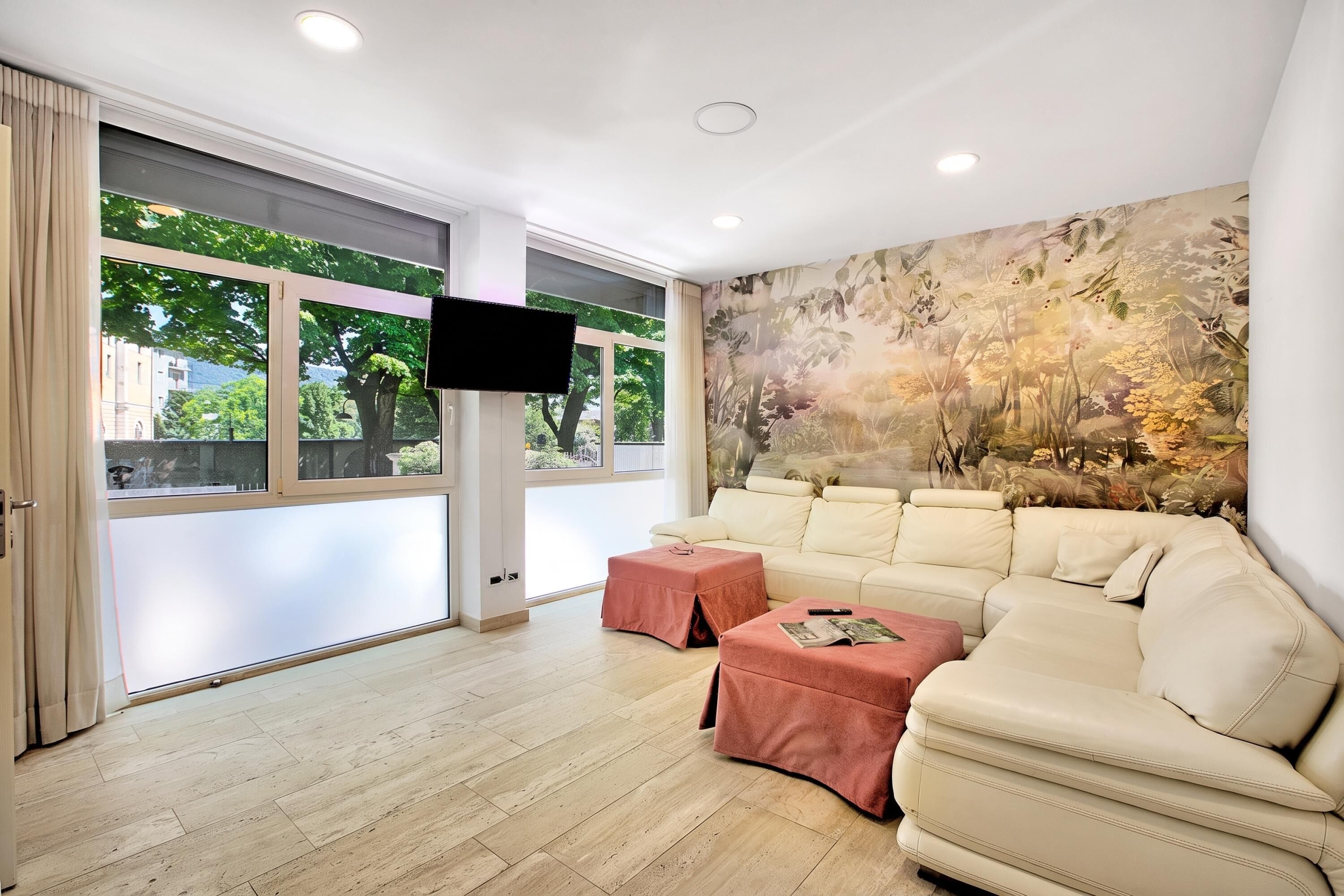 A modern living room with a beige sofa, a pink ottoman, and a large wall mural.