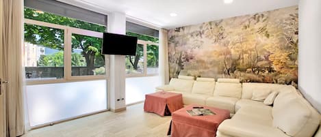 A modern living room with a beige sofa, a pink ottoman, and a large wall mural.