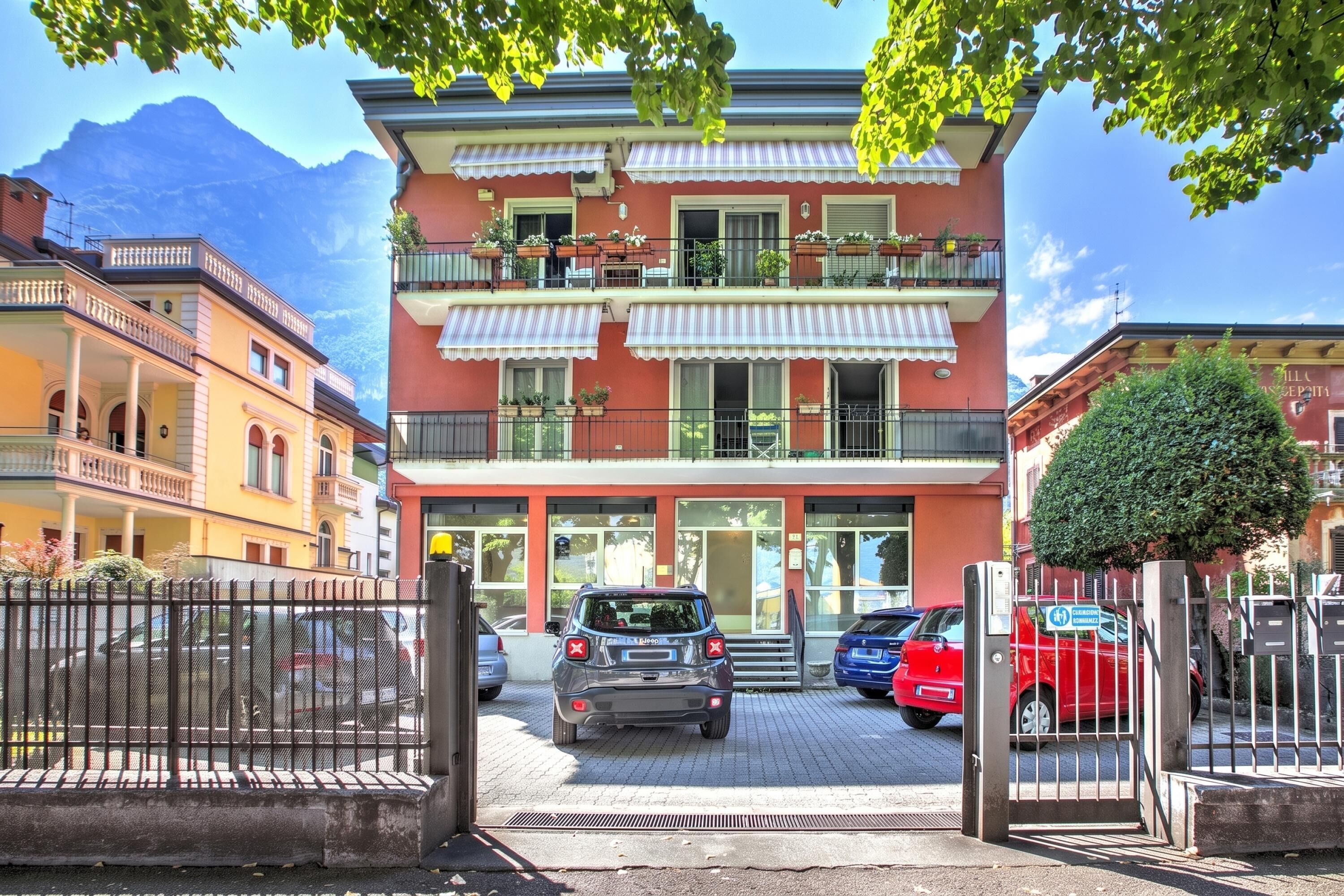 Ein mehrstöckiges Hotel mit roter Fassade, Balkonen mit Pflanzkübeln und einem Parkplatz mit Autos.