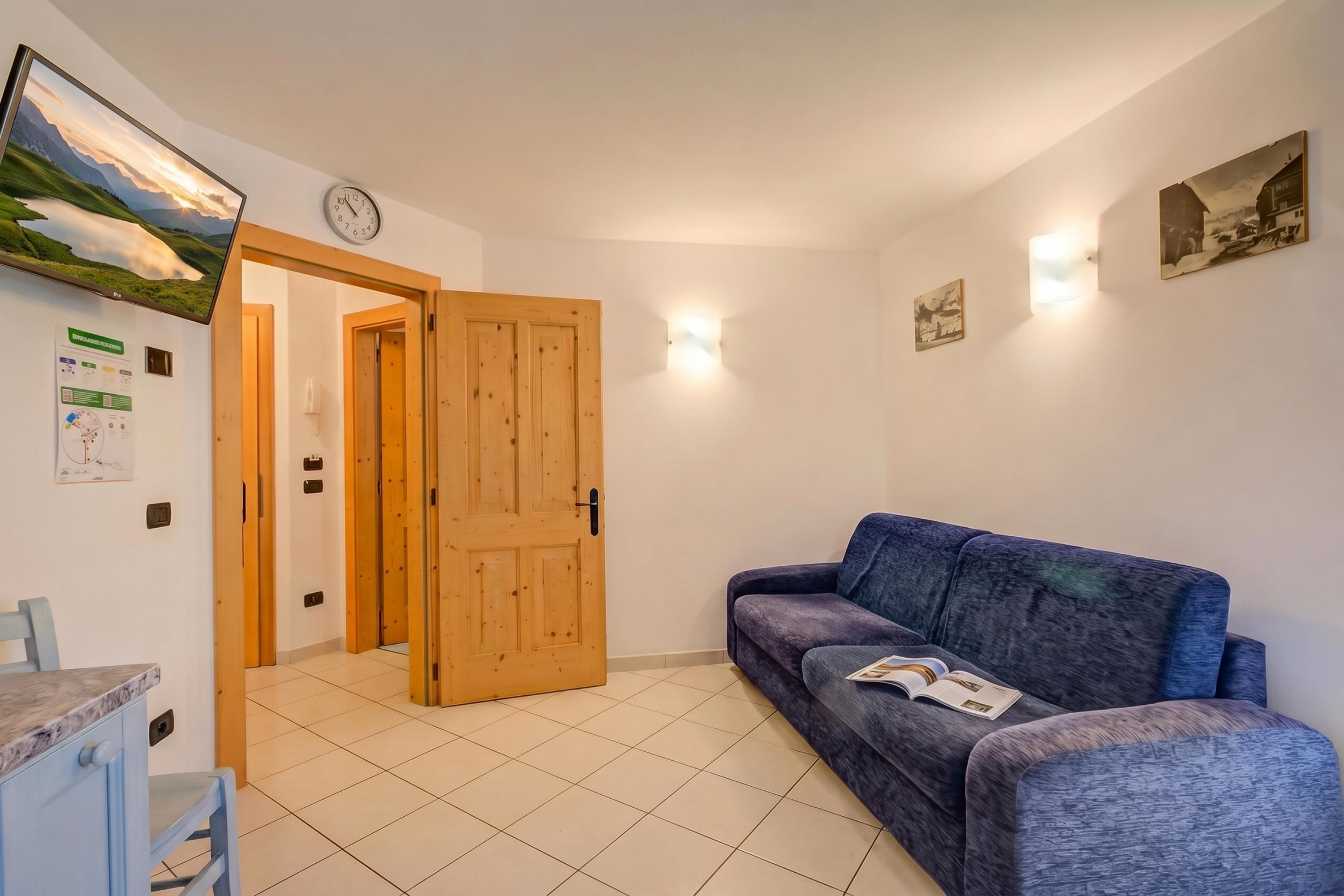 Un salon avec un canapé bleu, une porte en bois et une horloge fixée au mur.