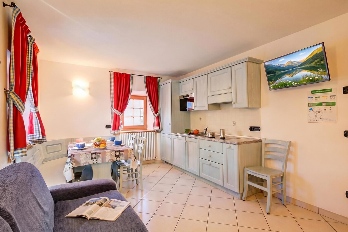 A compact living space with a dining area, kitchen, and a sofa with a magazine.
