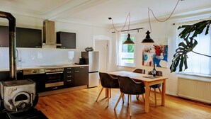 Una cocina moderna con estufa, horno y lavavajillas; un comedor con mesa y sillas; y un ventanal con una planta.