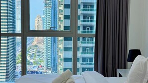 Een hotelkamer met een groot raam met uitzicht op de stad, een net opgemaakt bed met witte lakens, en het zichtbare logo van 'UZ HOMES'.