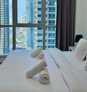 A hotel room with a large window, a bed with white linens, and a view of high-rise buildings.