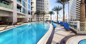 Una piscina con tumbonas, un edificio moderno y palmeras.
