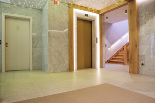 Un espacio moderno de ascensor con paredes de mármol, suelo de madera y una escalera que sube a otro piso.